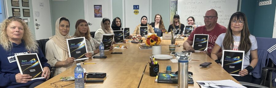 A diverse group of 11 adult learners proudly holding their books and smiling happily at the camera, celebrating their learning and achievements.