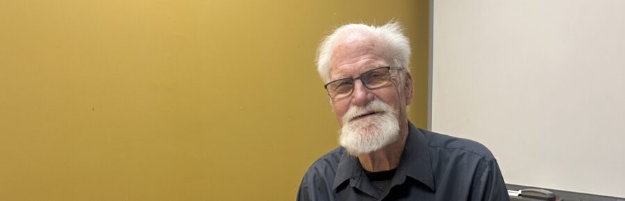 Photo of male volunteer Lonny with a warm relaxed smile, while he types on a laptop computer.